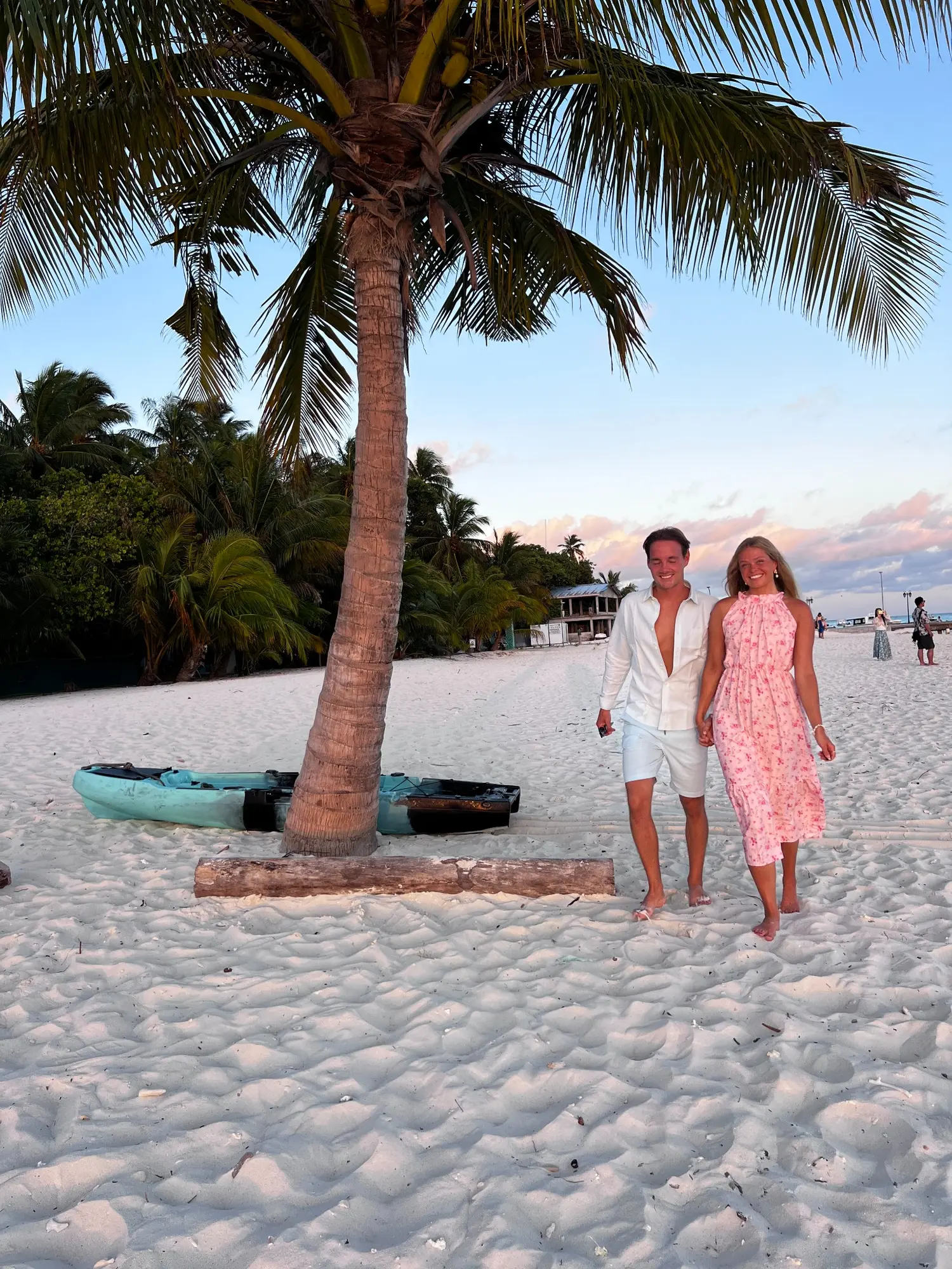 Jan and Emma walking barefoot beneath palm trees on a tropical beach
